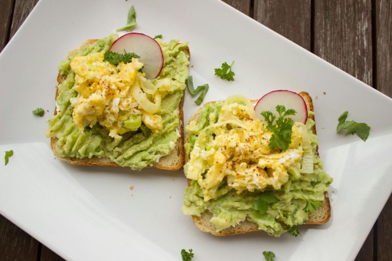 Image du petit-déjeuner savoureux avec toast à l’avocat et œufs brouillés, servi sur une assiette.